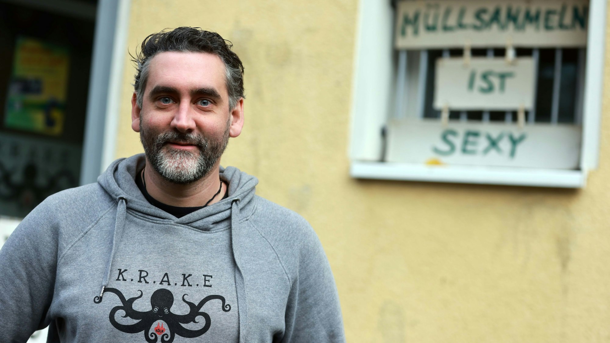 Christian Stock vor dem Müll-Museum der "Krake" in Humboldt/Gremberg, er trägt einen grauen Sweater mit der Zeichnung einer schwarzen Krake.