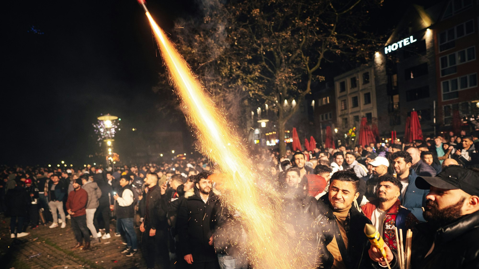 Funken sprühen aus einer Silvesterrakete, die ein Mann noch in der Hand hat und Richtung Nachthimmel hält.