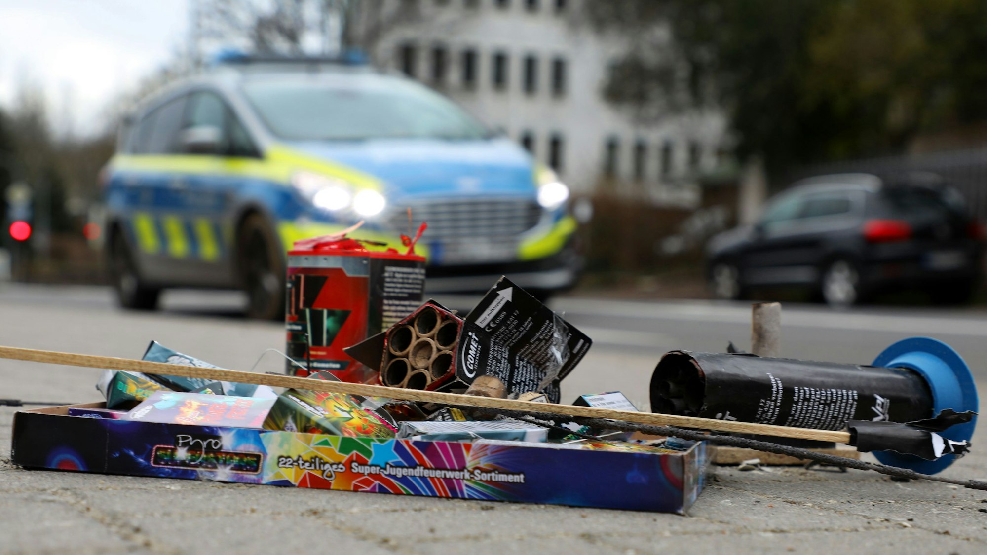 Feuerwerksreste liegen auf einem Gehweg an der Bergisch Gladbacher Hauptstraße. Dahinter fährt ein Polizeiauto auf der Straße.