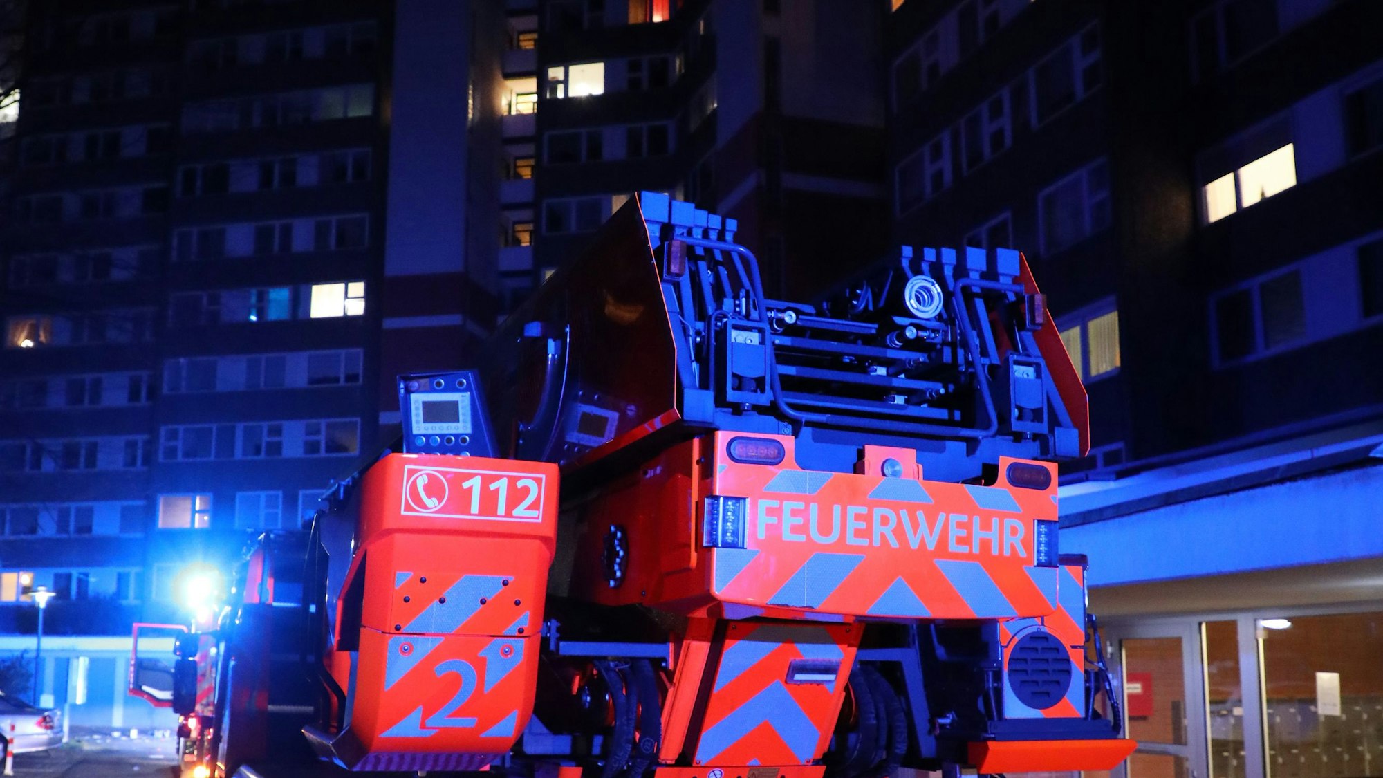 Ein Drehleiterfahrzeug steht in der Silvesternacht mit Blaulicht vor einem Hochhaus.
