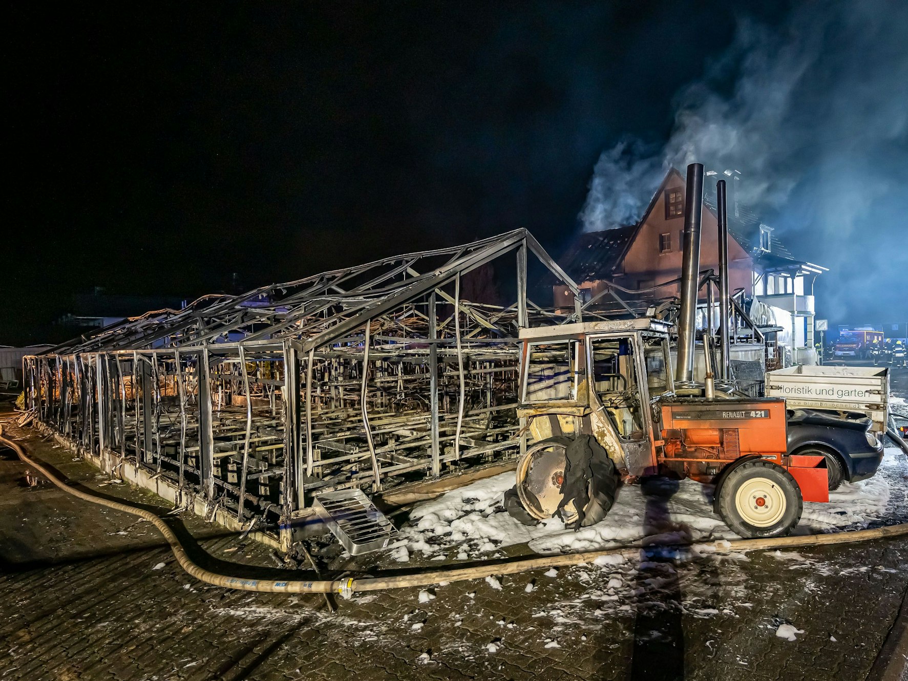 Zu sehen sind verkohlte Gewächshäuser und ein ausgebrannter Traktor.