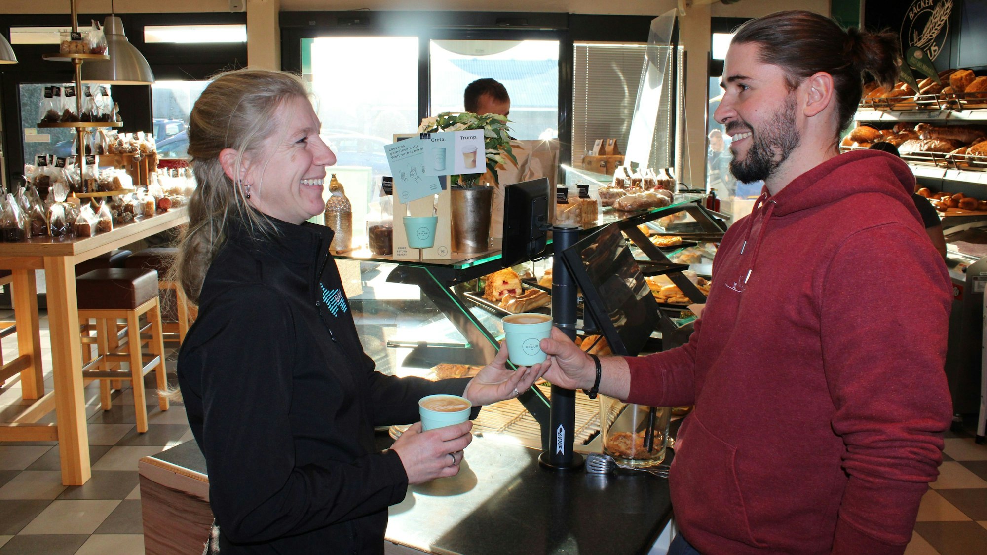 Zwei Mitarbeiter im Laden mit Recup Mehrwegbechern in der Hand.