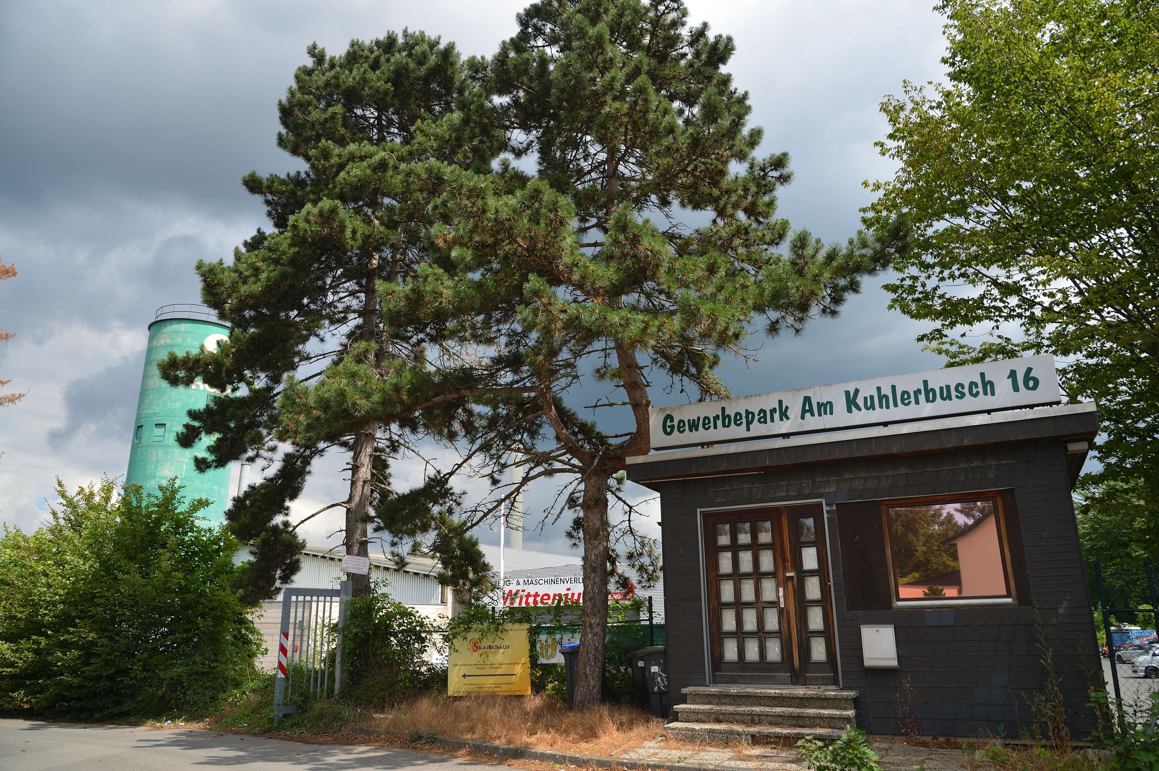 Ein Gebäude mit der Aufschrift „Gemwerbepark Am Kuhlerbusch 16“ neben einem Baum, im Hintergrund sind Firmengebäude zu sehen.