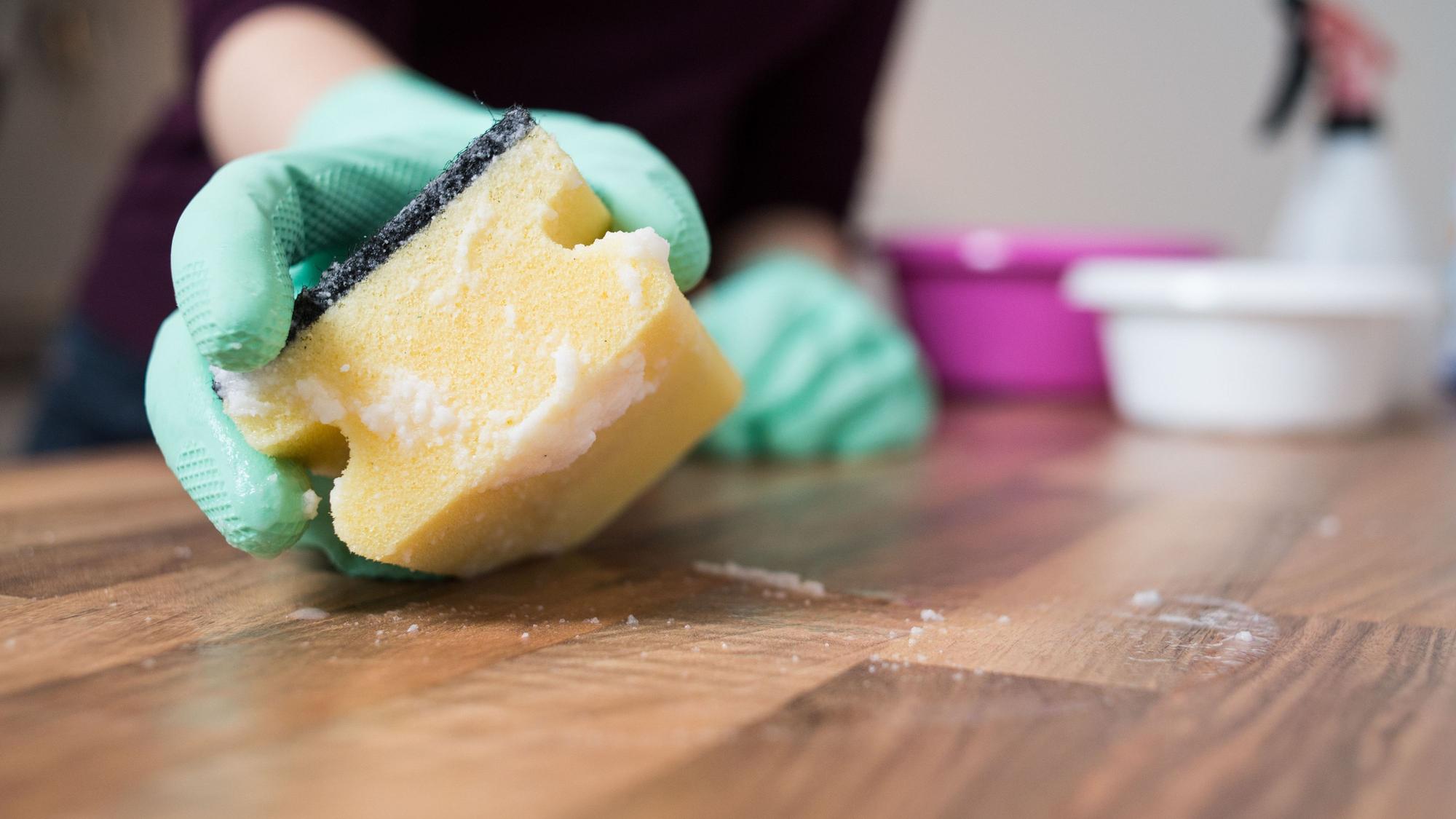 Zu sehen ist eine Hand in Gummihandschuh mit einem gelben Putzschwamm.