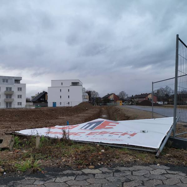 Wohnungsbau in Rheinbach: Ein Bauschild liegt umgestürzt auf einer Brachfläche.