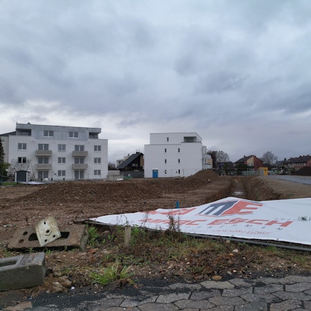 Wohnungsbau in Rheinbach: Ein Bauschild liegt umgestürzt auf einer Brachfläche.