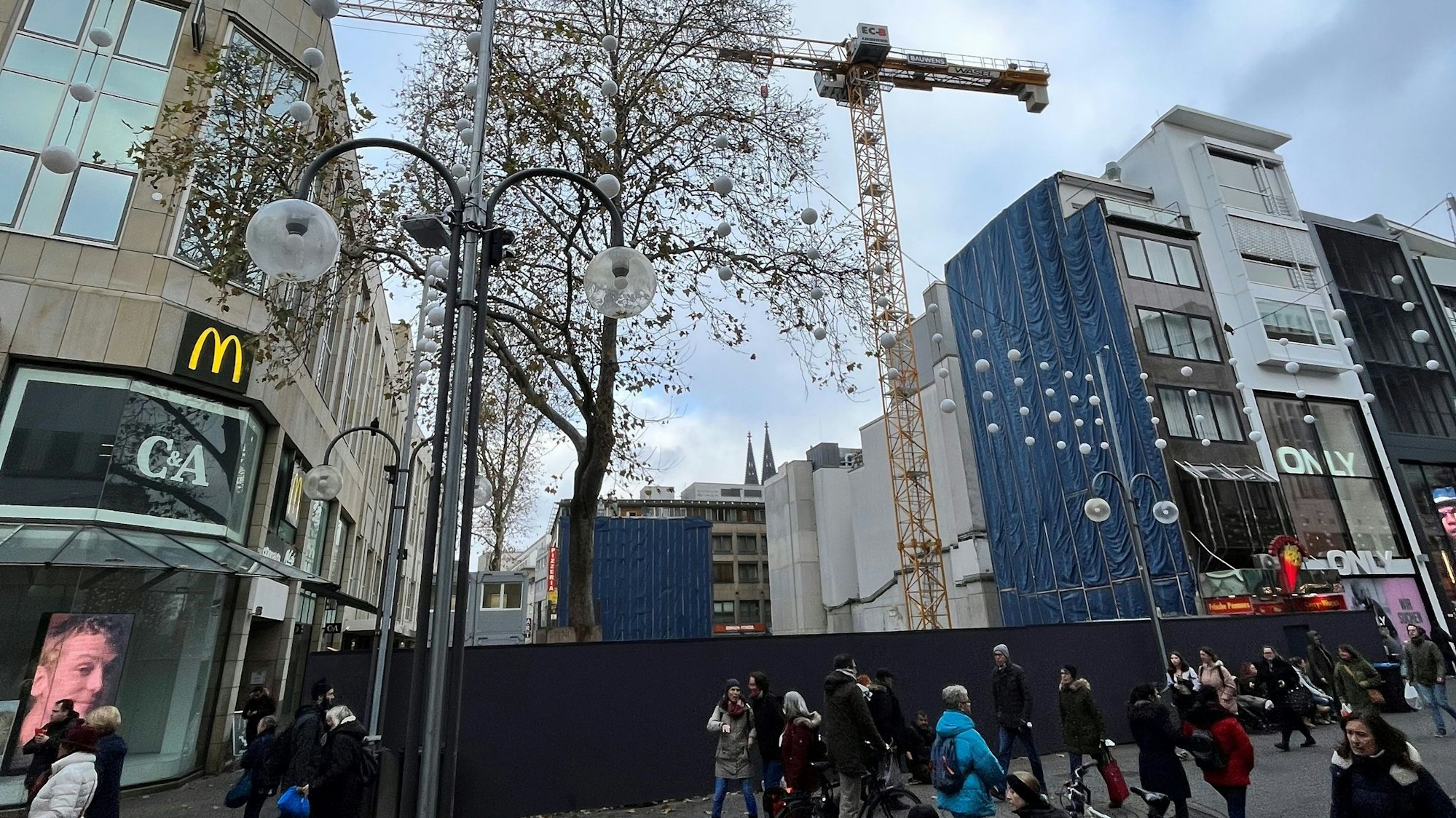 Die Baustelle an der Schildergasse mit blickdichtem Bauzaun. Ein Kran ragt dahinter in die Höhe.