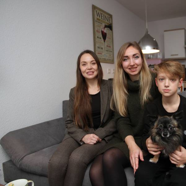 Die drei sitzen mit dem Chihuahua auf einem Sofa in ihrer Küche.