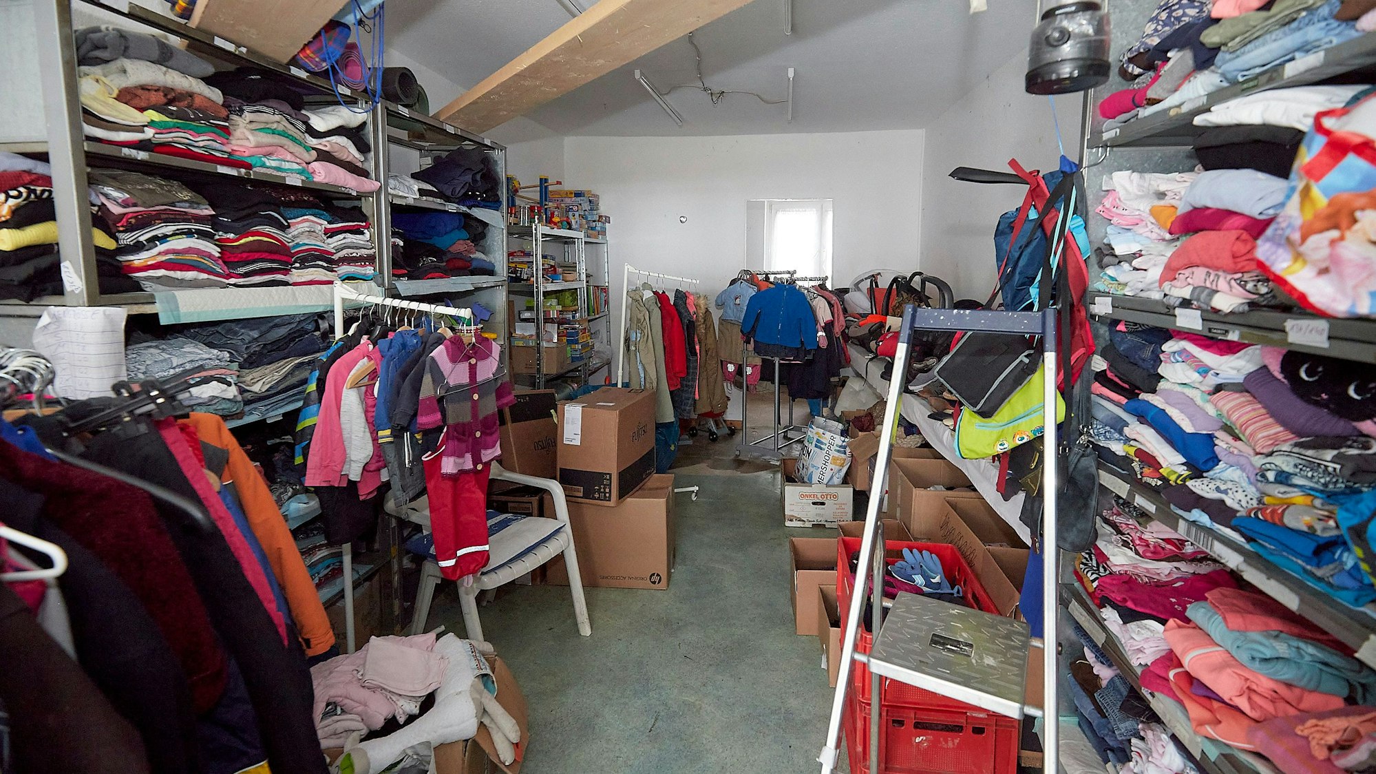 Zahlreiche Kleidungsstücke liegen in einem Spendenlager in Regalen.