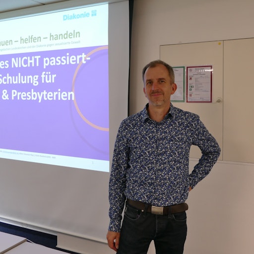 Christian Gröger steht vor einer Leinwand, an die projiziert steht: „Damit es NICHT passiert – Schulung für KSV & Presbyterien“.