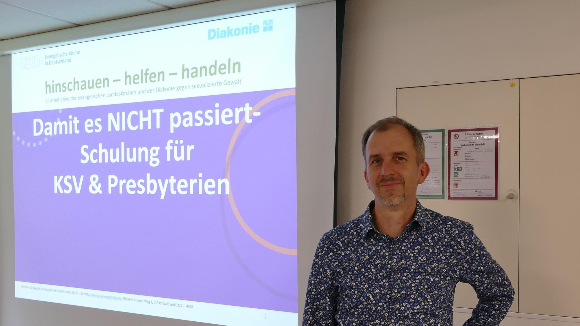 Christian Gröger steht vor einer Leinwand, an die projiziert steht: „Damit es NICHT passiert – Schulung für KSV & Presbyterien“.