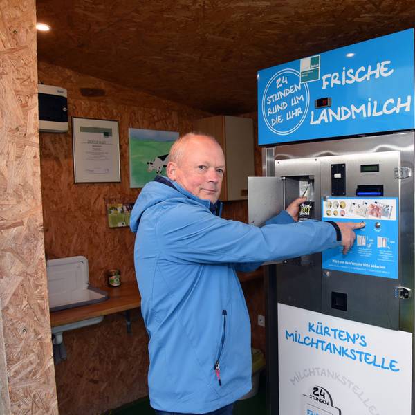 Ein Mann in einer blauen Jacke steht vor dem Milchautomat.