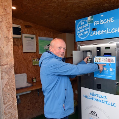 Ein Mann in einer blauen Jacke steht vor dem Milchautomat.