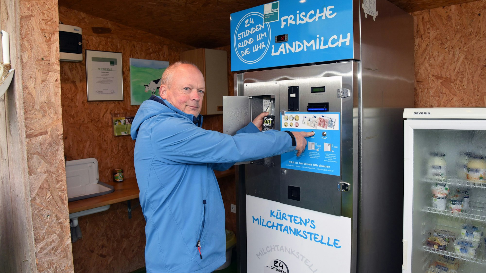 Ein Mann in einer blauen Jacke steht vor dem Milchautomat.