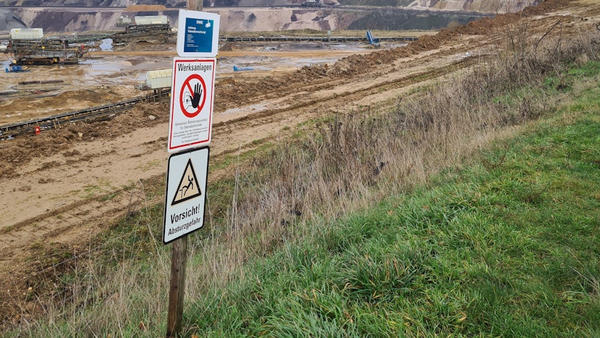 Der Tagebau Garzweiler. Im Vordergrund stehen Schilder, die zur Vorsicht mahnen.