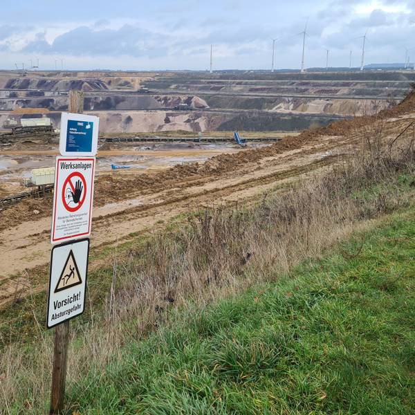 Der Tagebau Garzweiler. Im Vordergrund stehen Schilder, die zur Vorsicht mahnen.