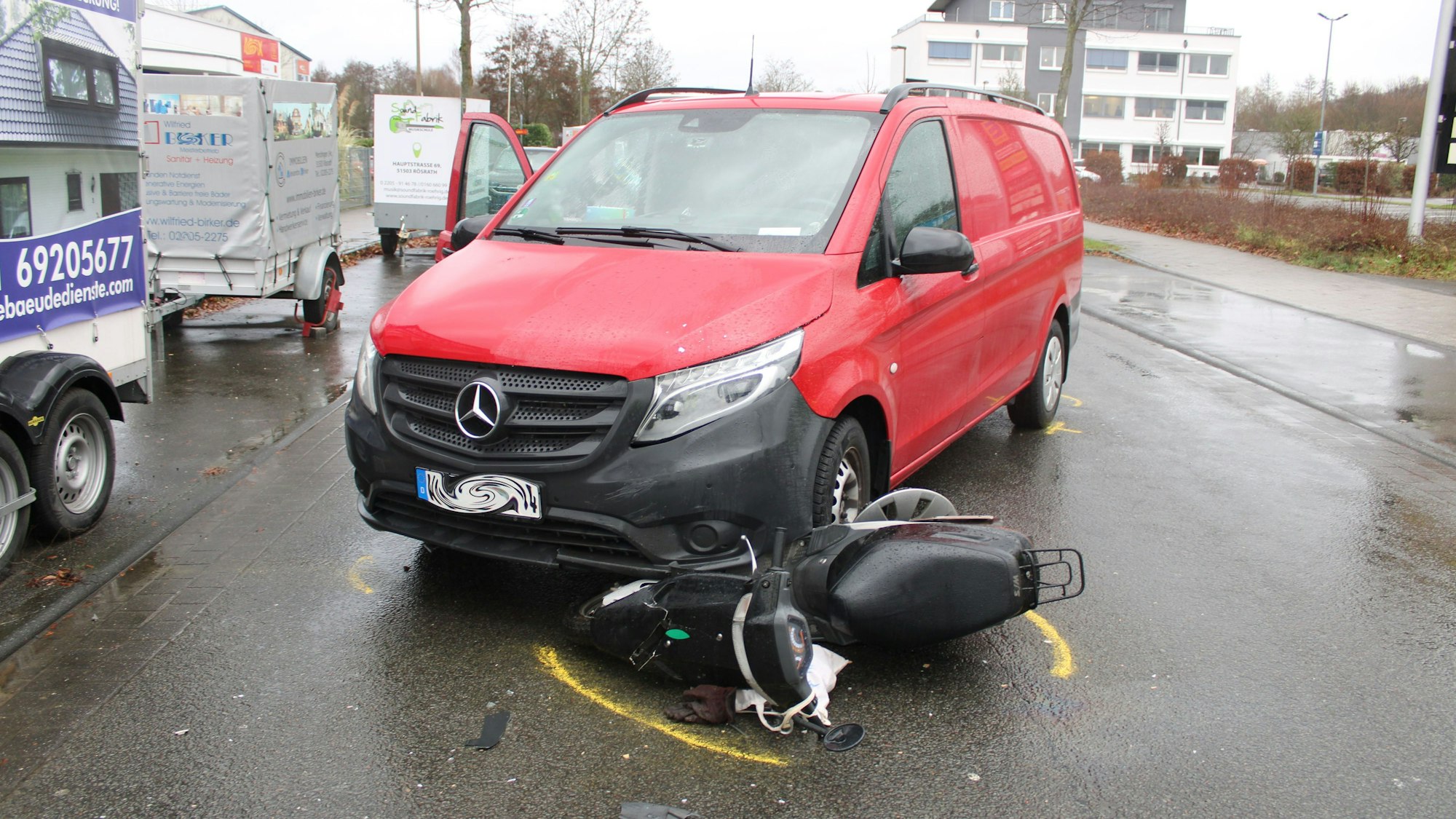 Ein Roller ist unter einem roten Mercedes-Transporter eingeklemmt.
