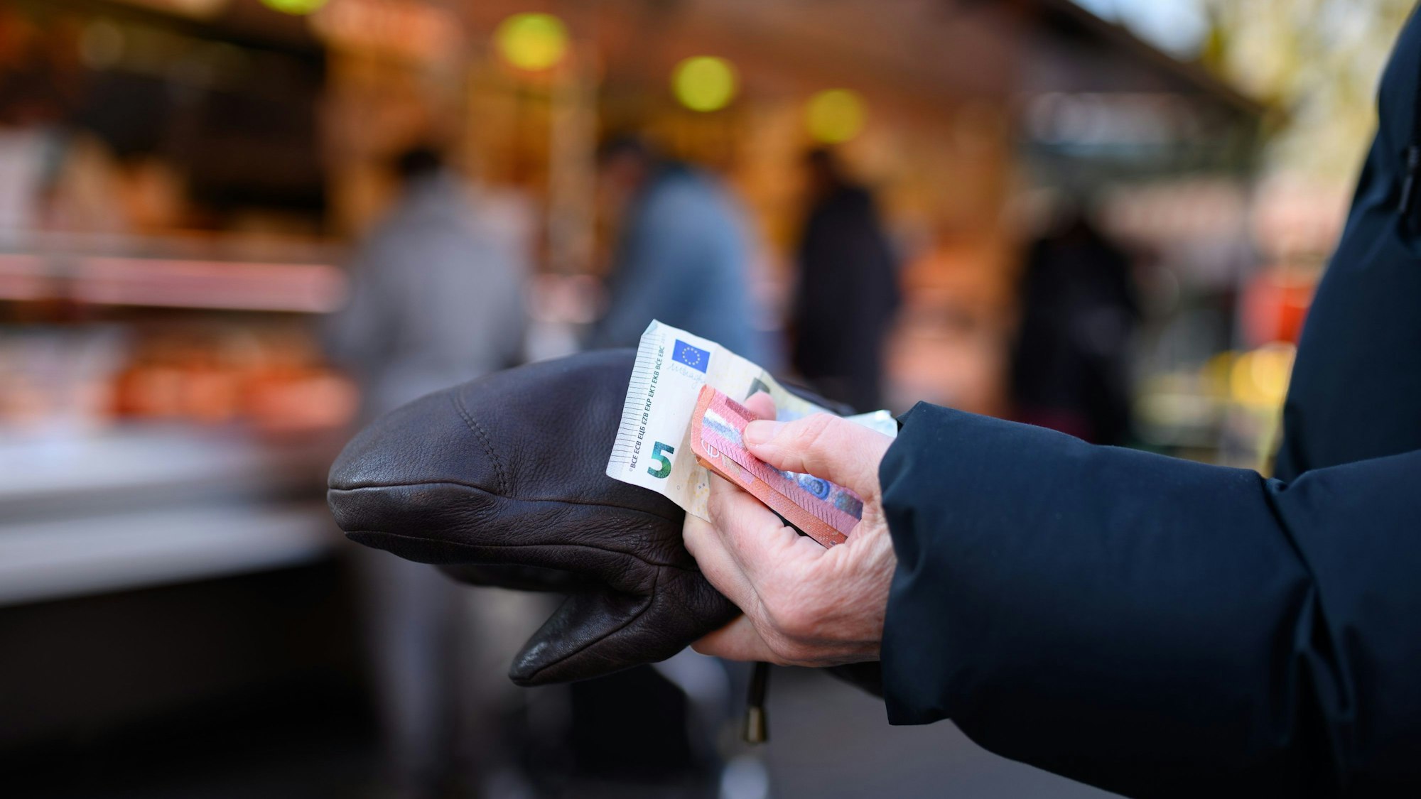 Eine Frau steht an einem Stand an und hält das Bargeld für ihren Einkauf in der Hand bereit.