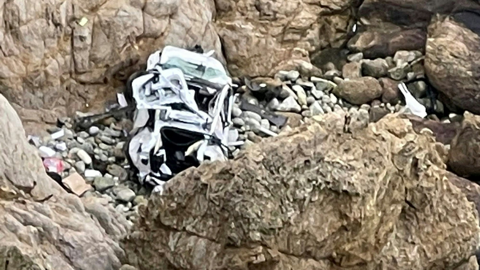 Ein völlig zerstörter weißer Tesla liegt in der Bucht „Devils Slide“ in Kalifornien. Ein Helikopter muss die Insassen retten.