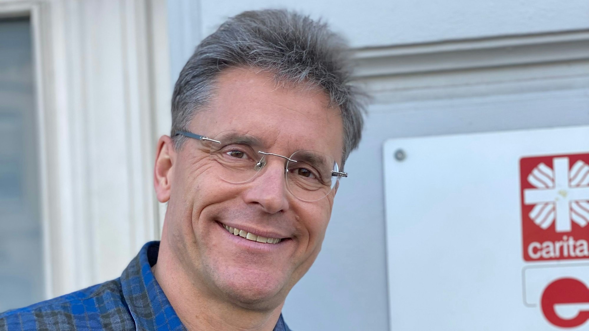 Ralf Klaes steht vor einer Wand, an der ein Schild der Caritas zu erkennen ist.
