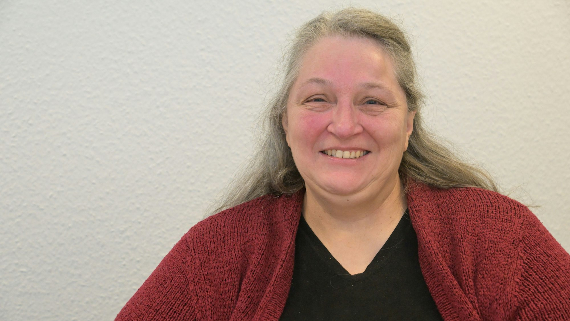 Monika Friedrichs brustaufwärts lächeldn vor einer weißen Wand.