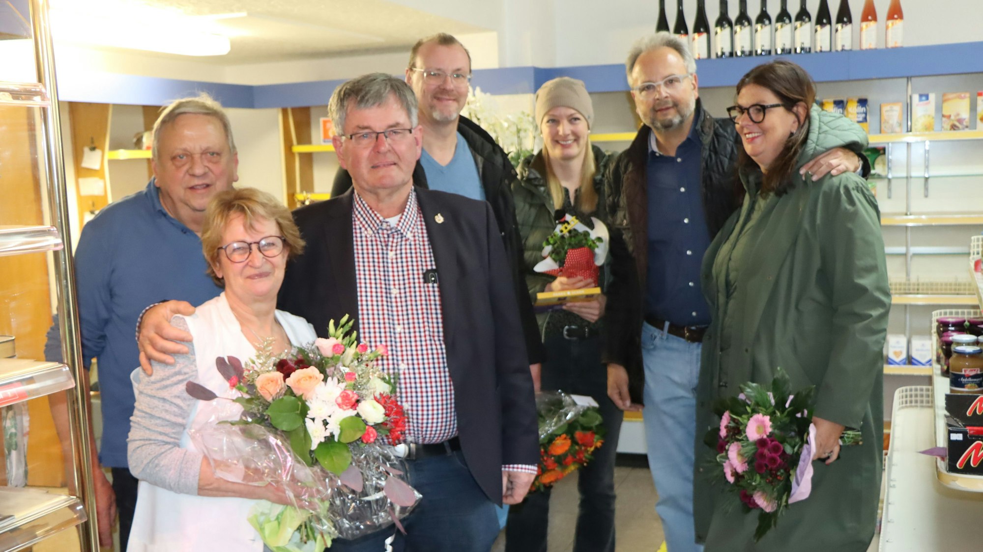 Ortsvorsteher Willi Winkelhag (3.v.l.) steht zusammen mit Harald und Bernadette Seidel und weiteren Personen in dem inzwischen fast leer geräumten Laden. Frau Seidel hält einen Blumenstrauß
