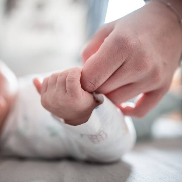 Ein Baby klammert sich an den Finger seiner Mutter.