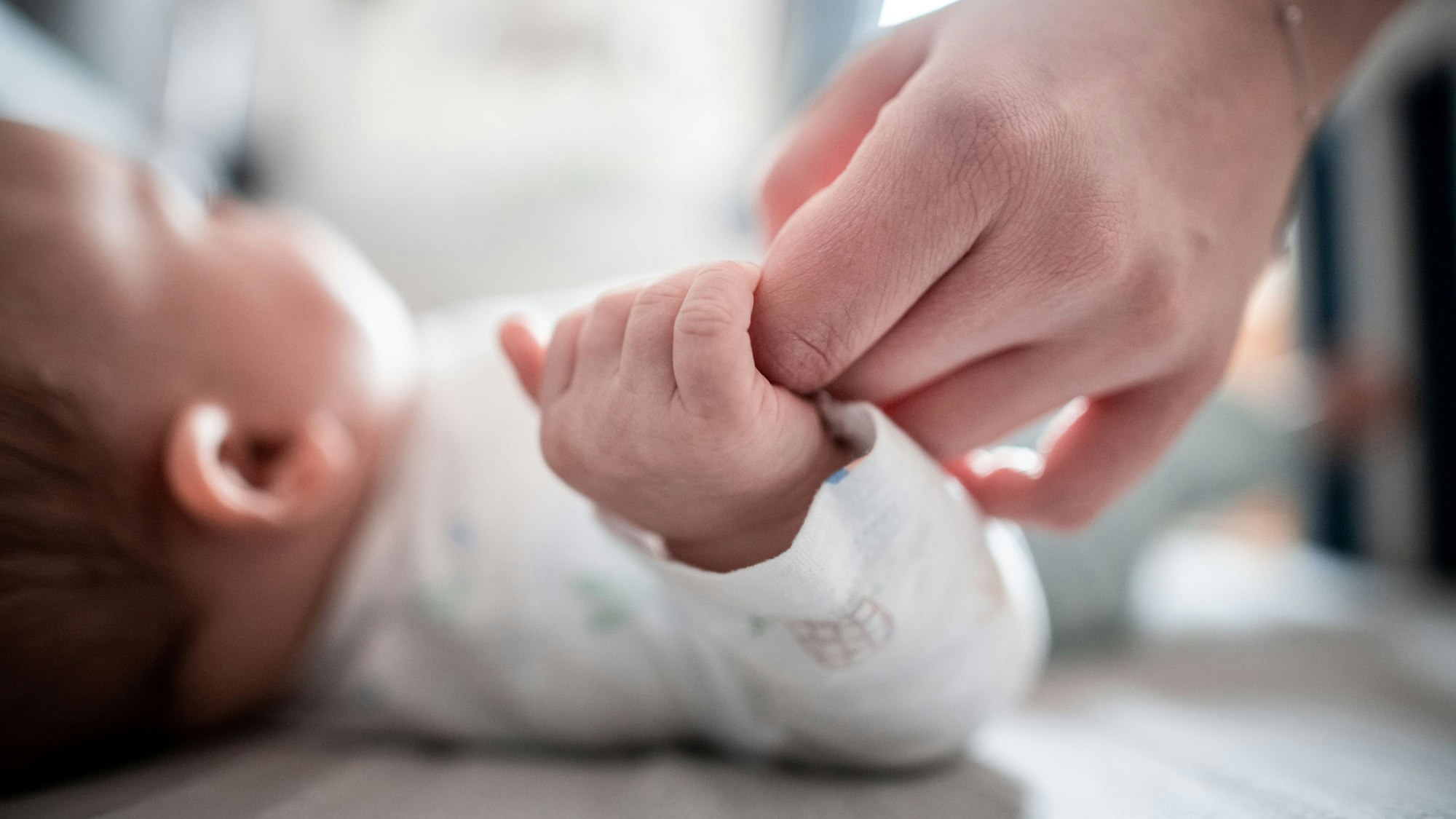Ein Baby klammert sich an den Finger seiner Mutter.
