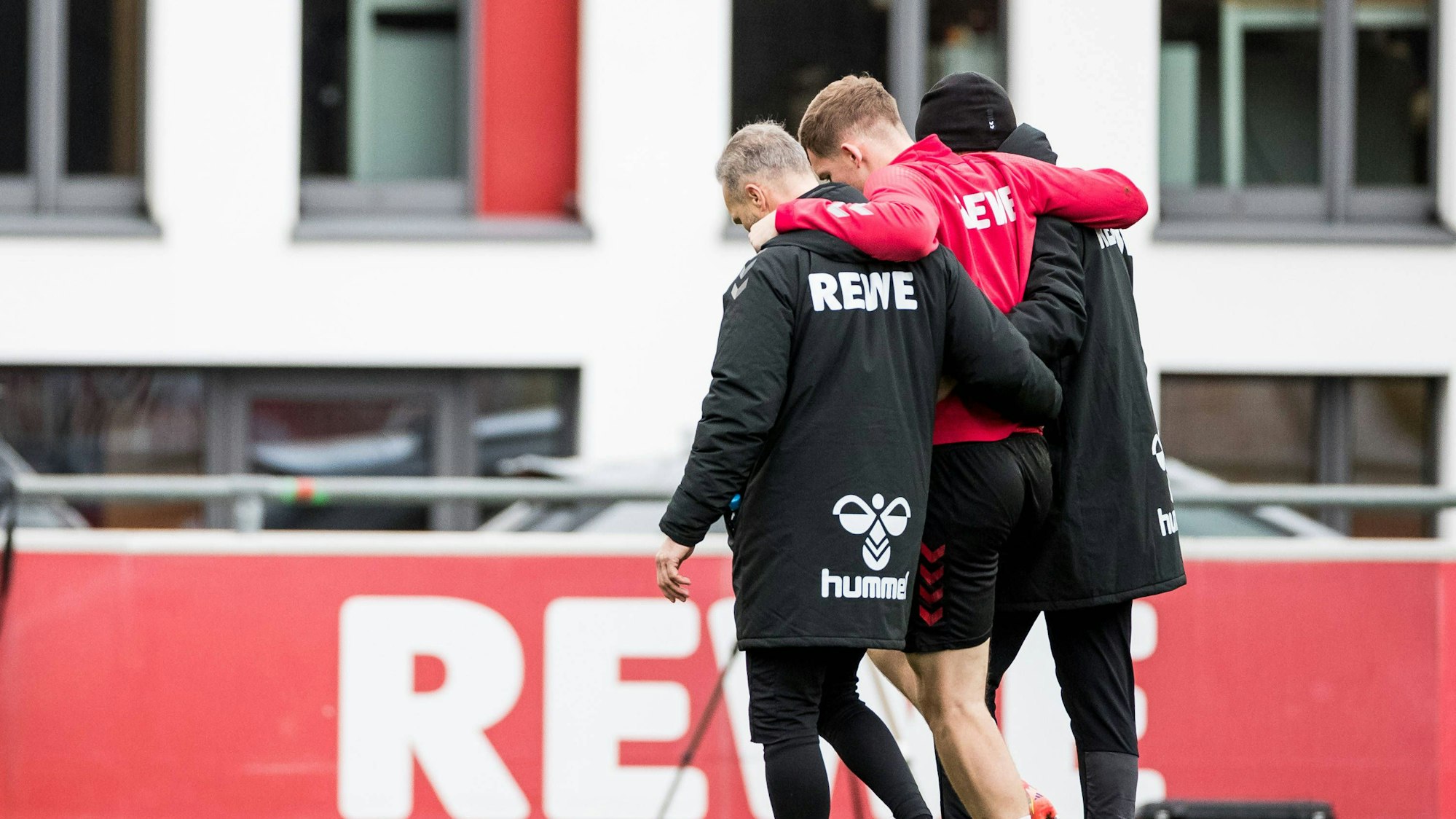 Luca Kilian wird vom Physio Marvin Kreuzwieser (r.) und Torwart-Trainer Uwe Gospodarek verletzt vom Platz begleitet.