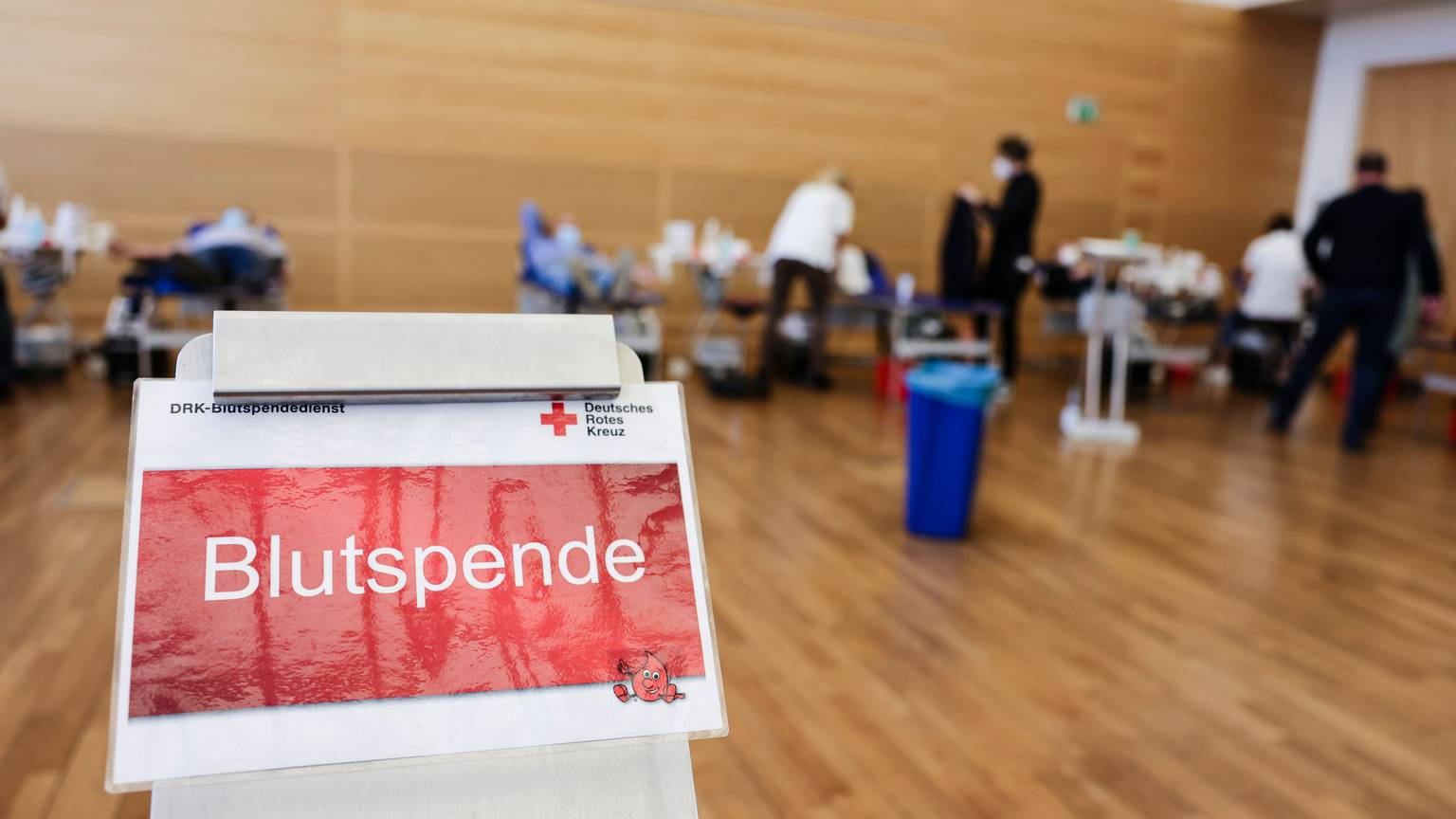 Ein Schild mit der Aufschrift „Blutspende“. Im Hintergrund sind mehrere Liegen aufgebaut.