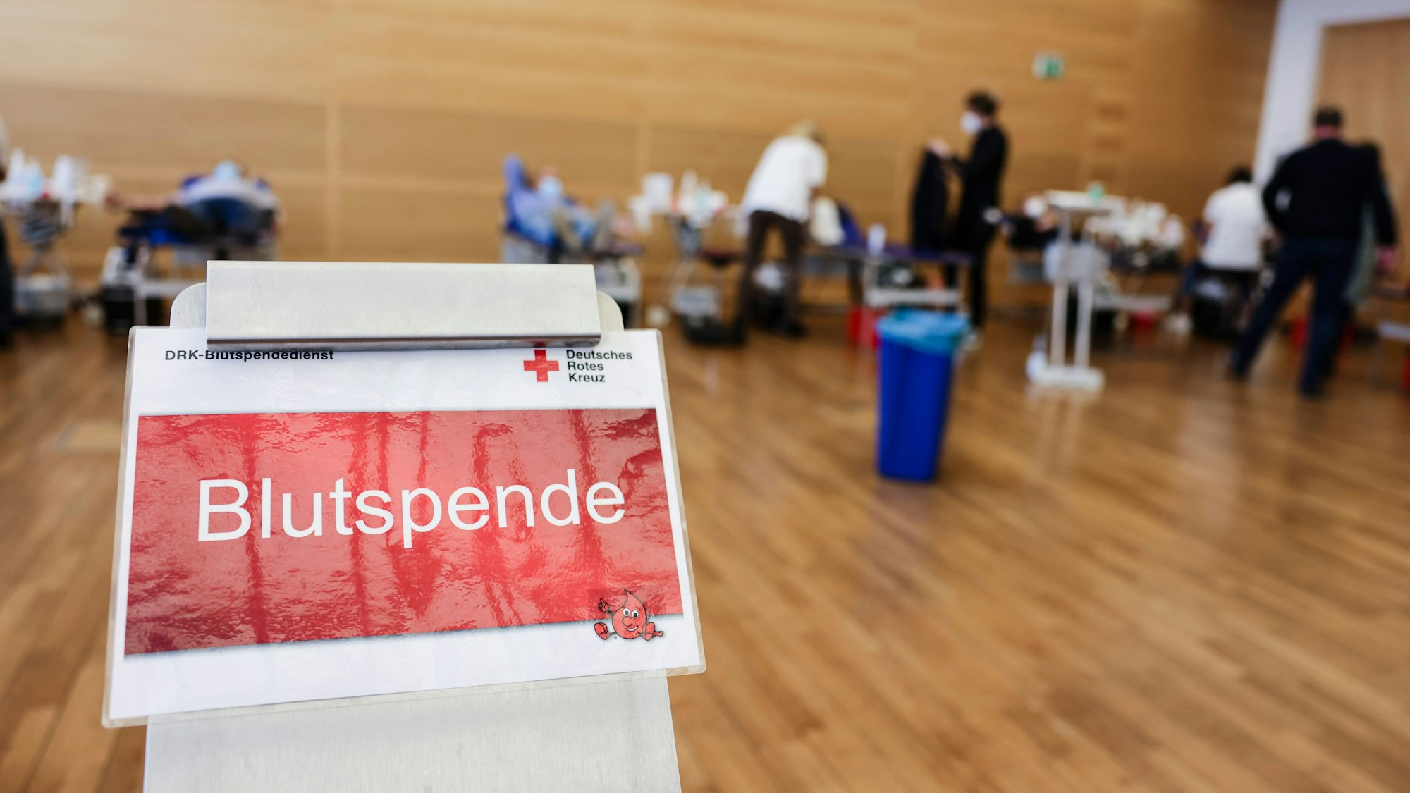 Ein Schild mit der Aufschrift „Blutspende“. Im Hintergrund sind mehrere Liegen aufgebaut.