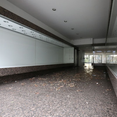 Vor den Eingang eines Geschäftes an der Hauptstraße, dessen Auslagen hinter den Fensterfronten leer sind, hat der Wind Laub geweht.