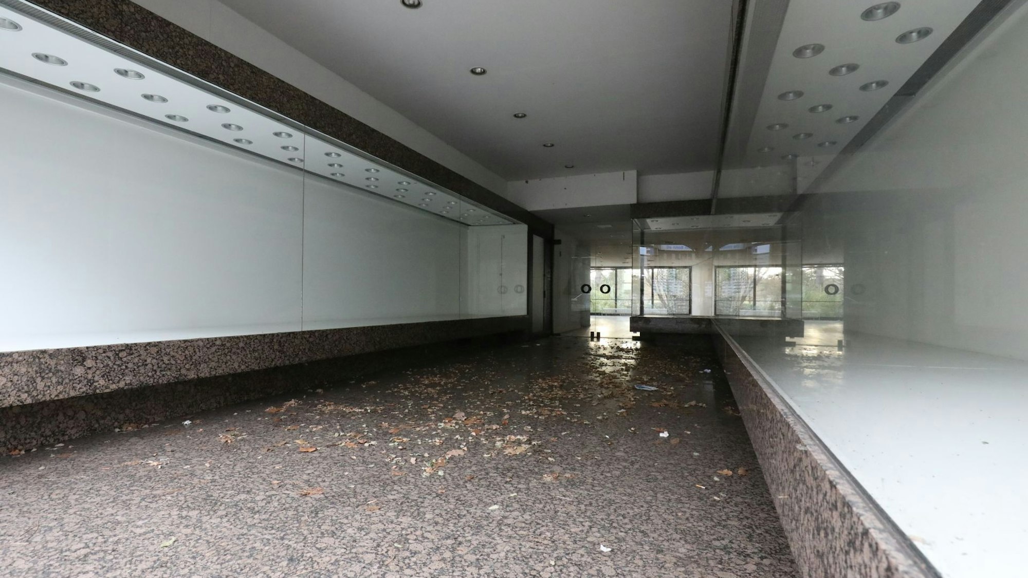 Vor den Eingang eines Geschäftes an der Hauptstraße, dessen Auslagen hinter den Fensterfronten leer sind, hat der Wind Laub geweht.