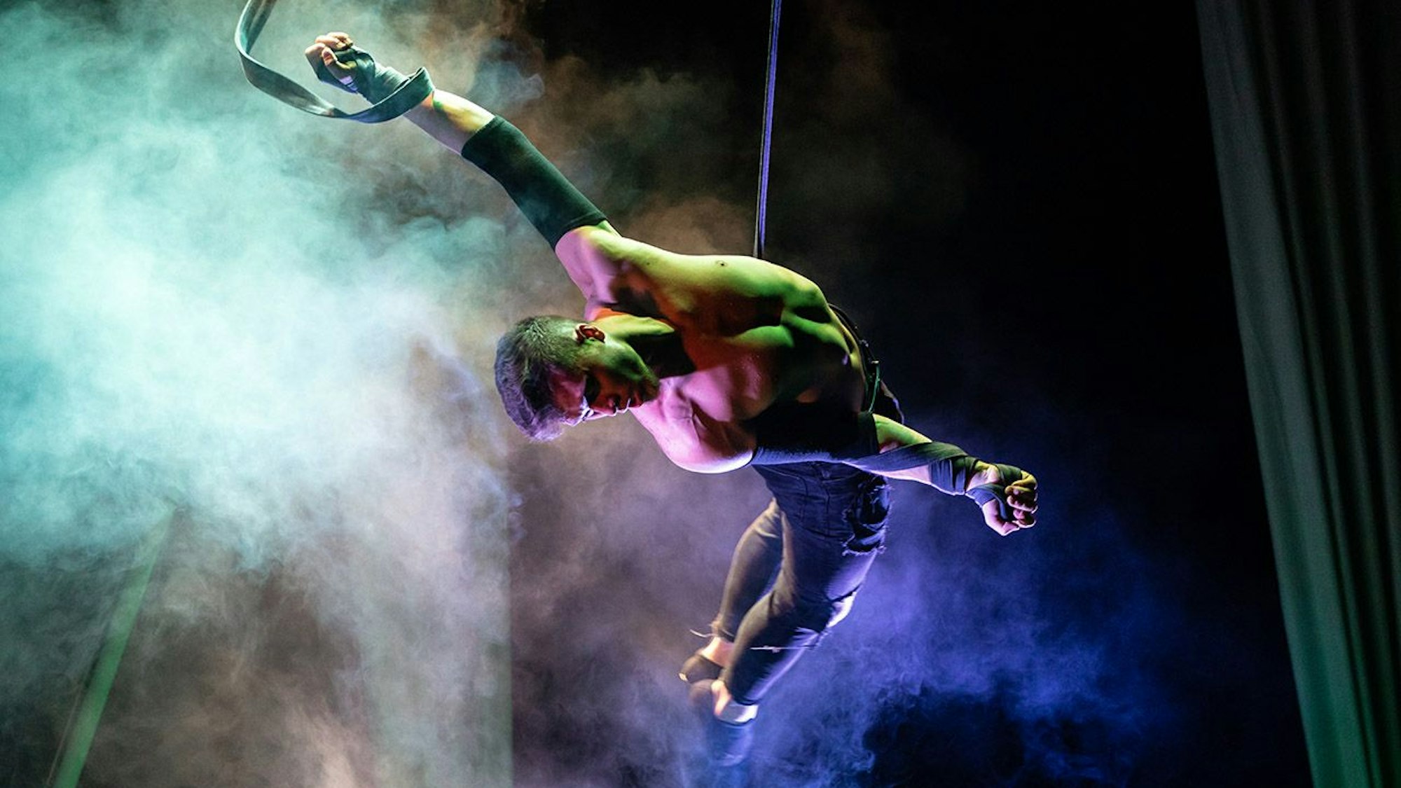 Ein Akrobat hängt an seidenen Tüchern von der Decke.