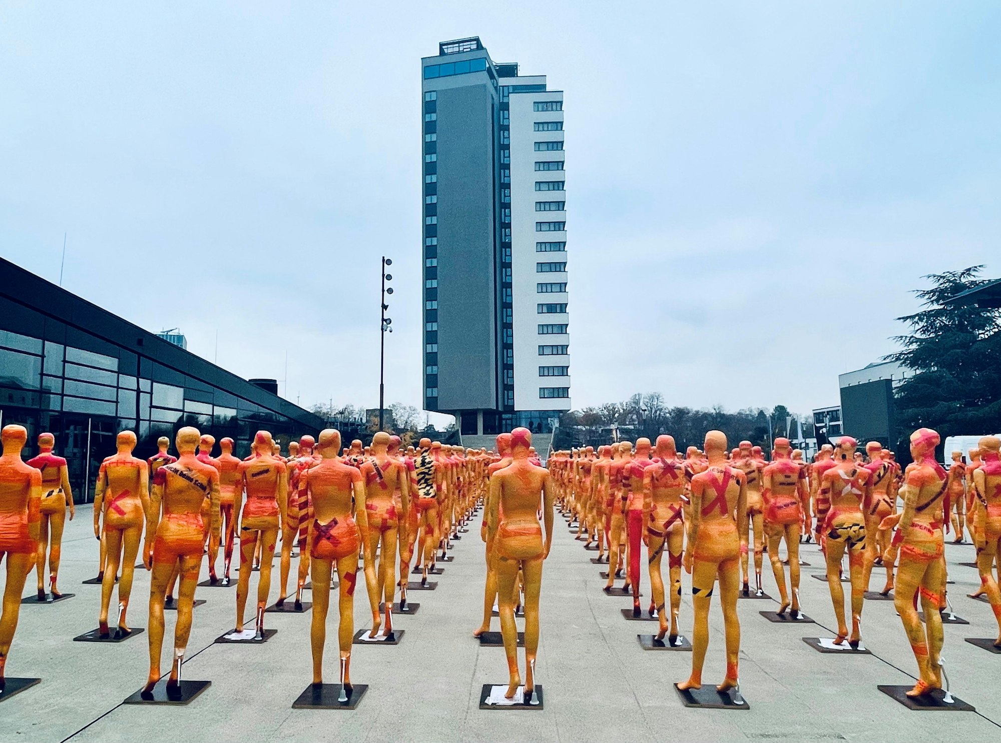 Kunstinstallation des Künstlers Meseg in Bonn zum Orange Day 2022 auf dem Platz der Vereinten Nationen: Sichtbar sind orangefarbene Körper, symmetrisch aufgestellt in langen Reihen.