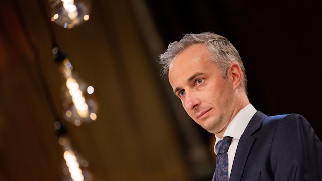 Jan Böhmermann steht in einem dunklen Anzug mit blauer Krawatte und weißem Hemd auf einer Bühne.