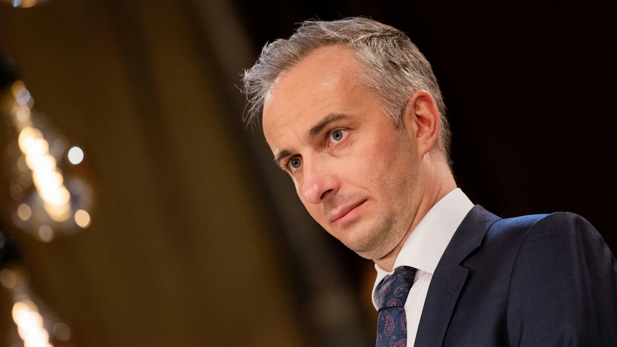Jan Böhmermann steht in einem dunklen Anzug mit blauer Krawatte und weißem Hemd auf einer Bühne.