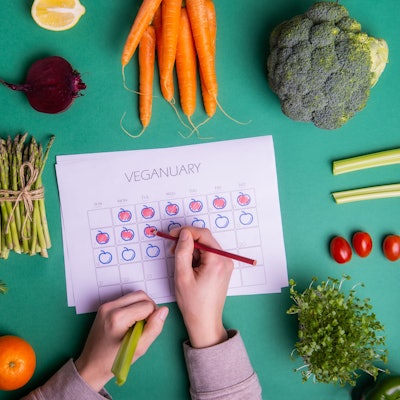 Jemand füllt einen Veganuary-Plan aus, darum liegt verschiedenen Obst und Gemüse.