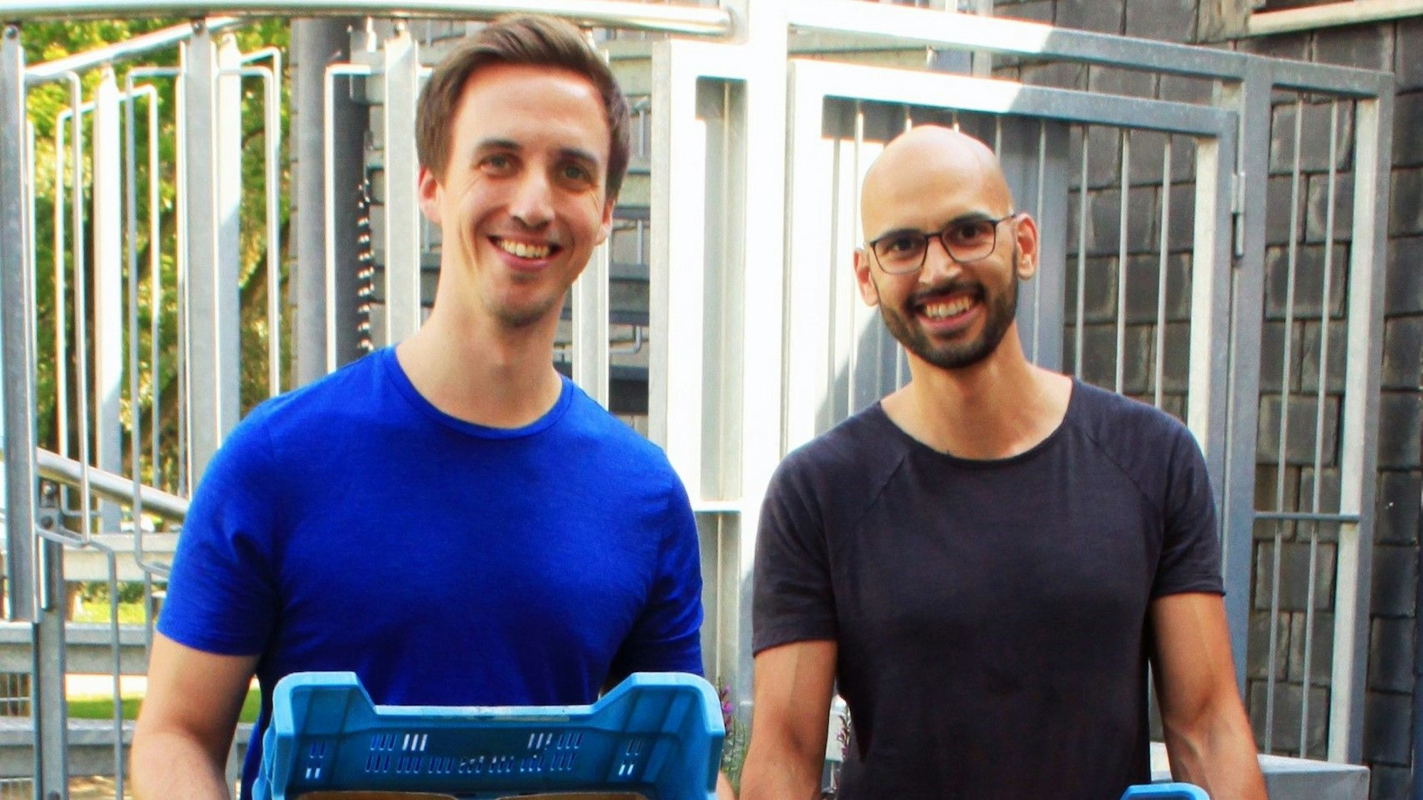 Johannes Decker und Daniel Neumann halten Gemüsekisten in den Händen und lächeln in die Kamera.