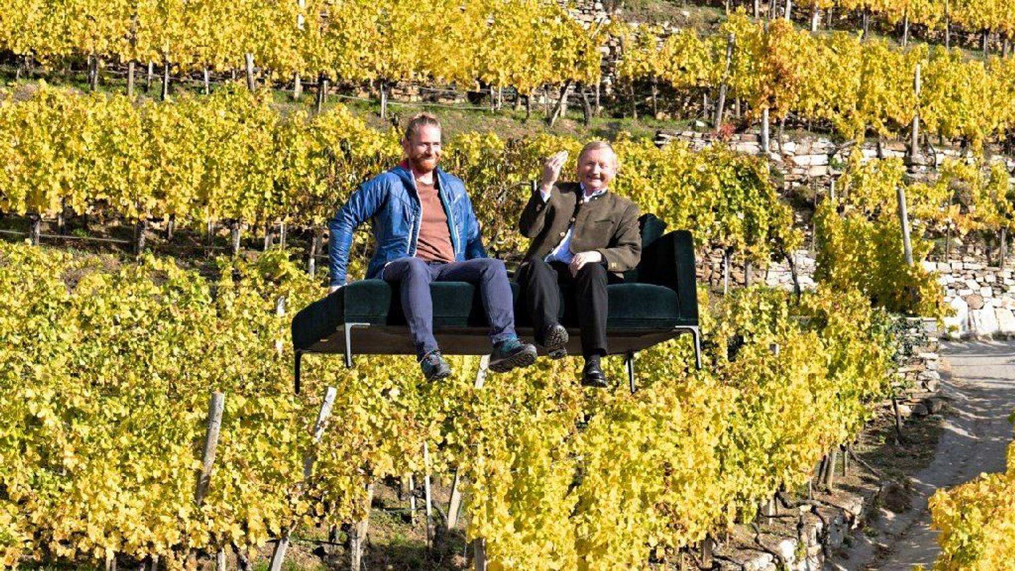 Zwei Menschen sitzen auf einem Sofa, das vor einem Weinberg schwebt.