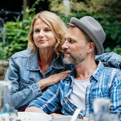 Ein Paar mittleren Alters sitzt bei einem Grillfest nah beieinander.