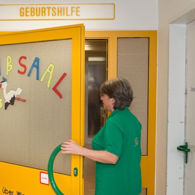 Eine Hebamme betritt auf der Geburtshilfestation im Krankenhaus Gummersbach einen Kreißsaal. Auf dem Zugang klebt ein aus Papier ausgeschnittener Storch.