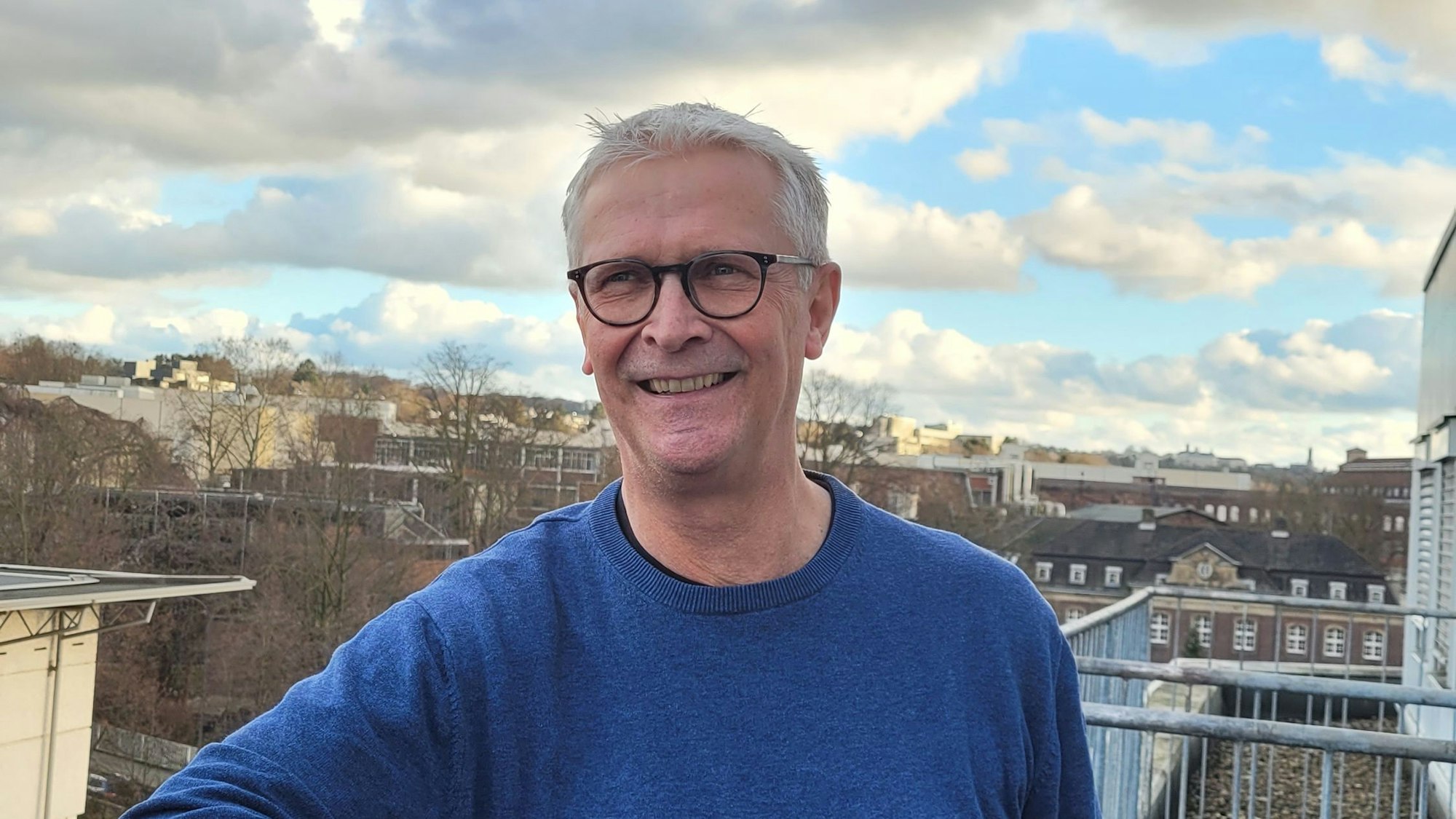 Heribert Hölzer, Sieger Fotowettbewerb 2022, steht an einem Geländer, im Hintergrund ist Bergisch Gladbach zu sehen.