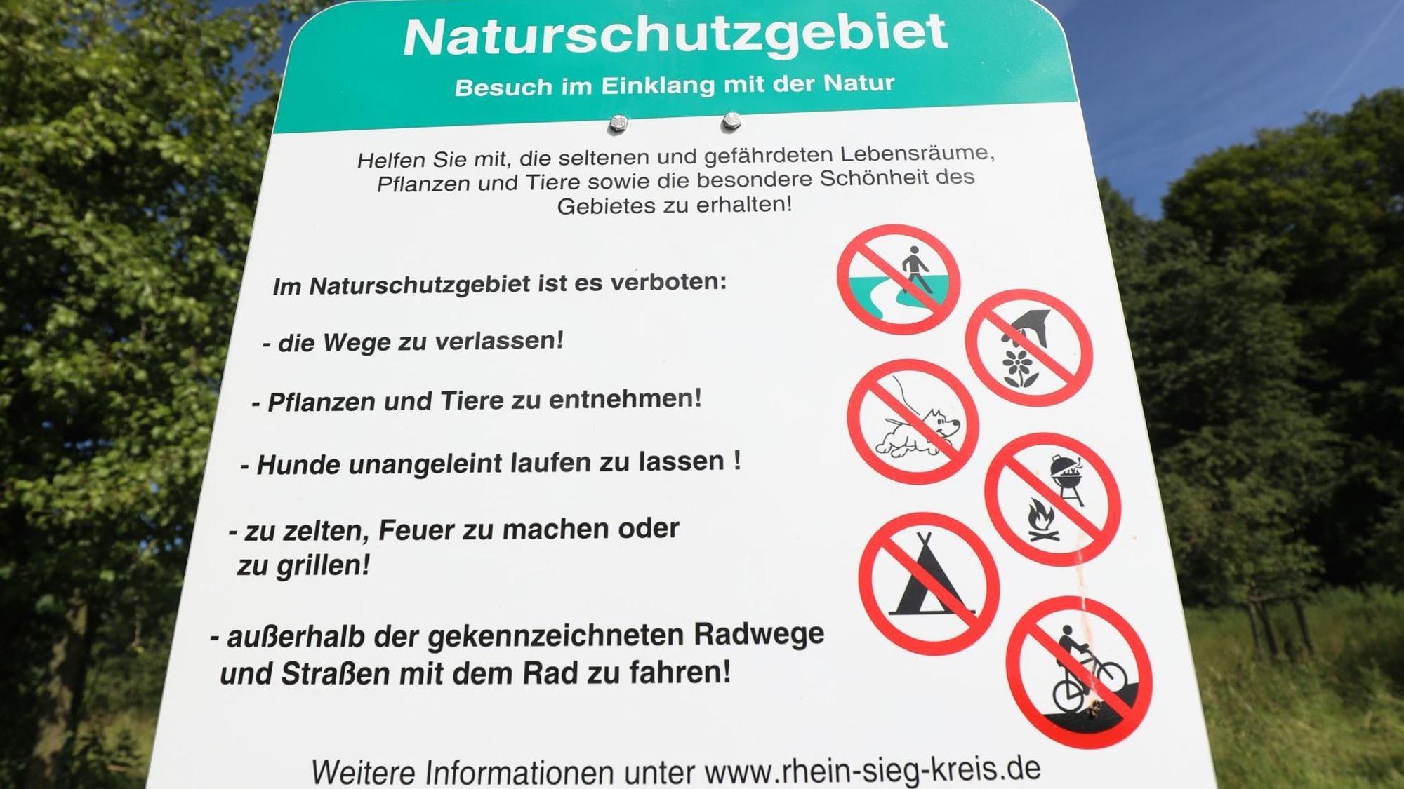 Ein Schild zeigt rot-weiße Piktogramme, mit denen Verbote wie Zelten oder das Verlassen der Wege bildlich gemacht werden.
