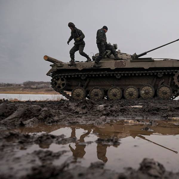 Zwei ukrainische Soldaten stehen während einer Schießübung auf einem Panzer, der auf einem Feld voller Pfützen steht.