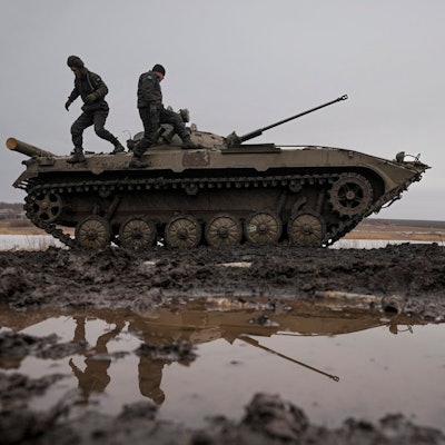 Zwei ukrainische Soldaten stehen während einer Schießübung auf einem Panzer, der auf einem Feld voller Pfützen steht.