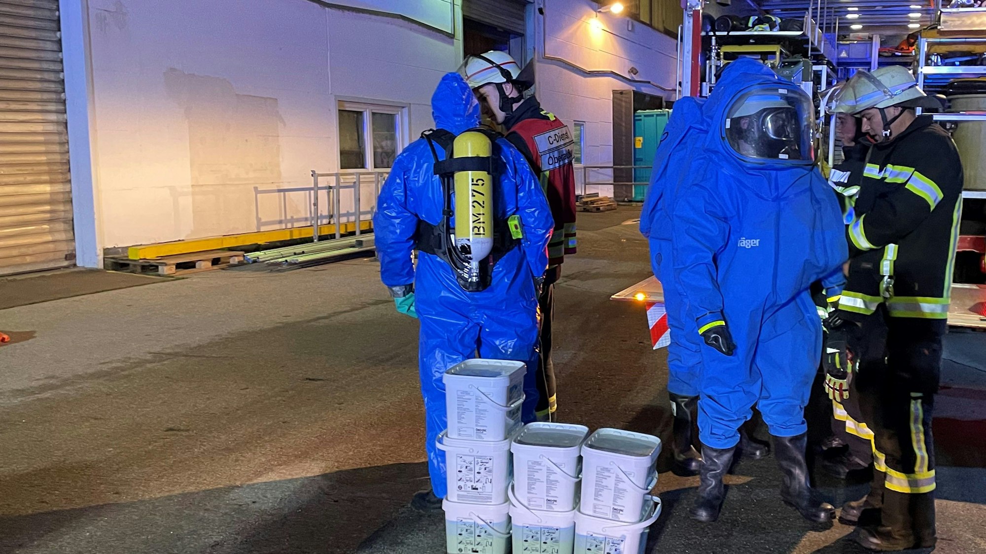 Feuerwehrleute in blauen Anzügen und mit Atemschutz stehen vor einer Halle.