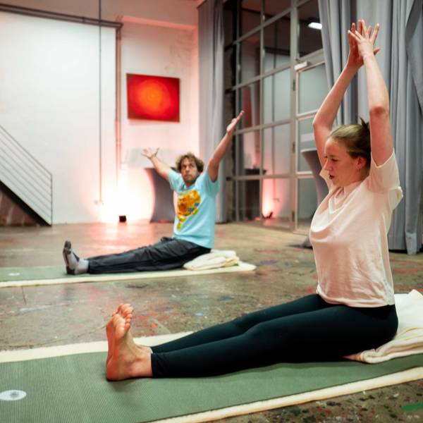 Tom Steinicke und Stella Wolters sitzen auf Yoga-Matten und machen eine Übung.