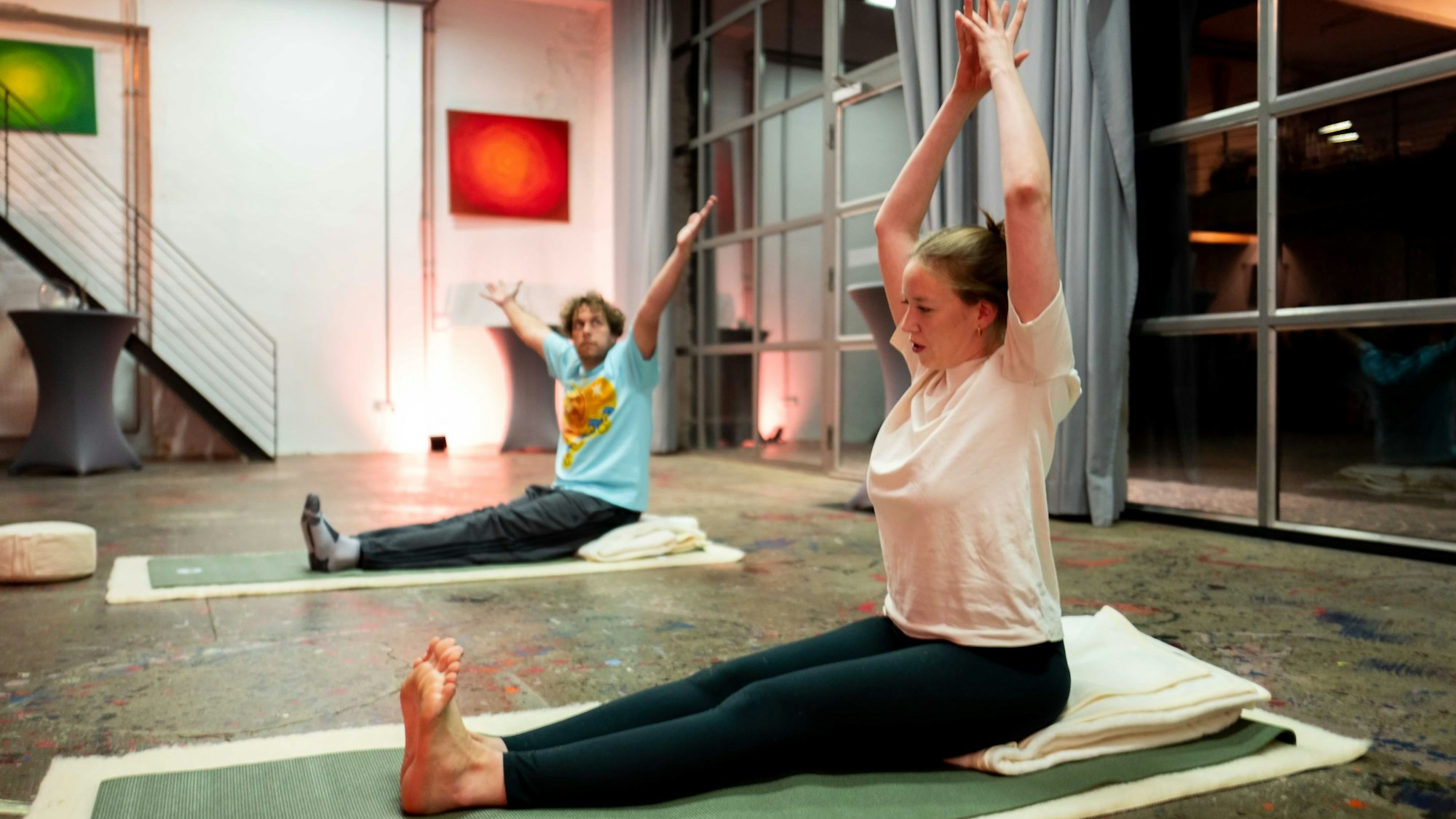 Tom Steinicke und Stella Wolters sitzen auf Yoga-Matten und machen eine Übung.