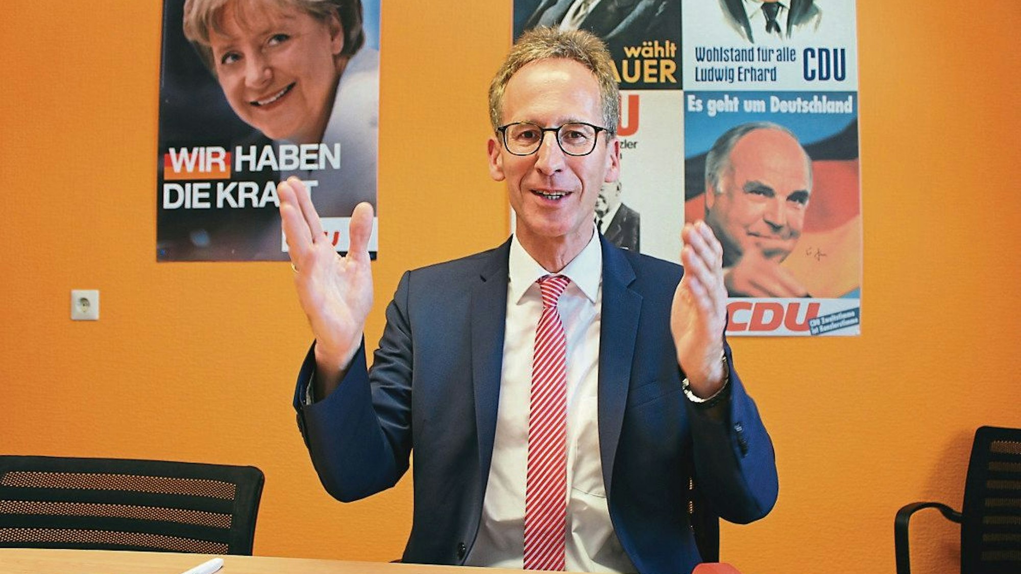 Detlef Seif sitzt am Tisch, an der Wand hängen alte CDU-Wahlplakate mit Angela Merkel und Helmut Kohl.